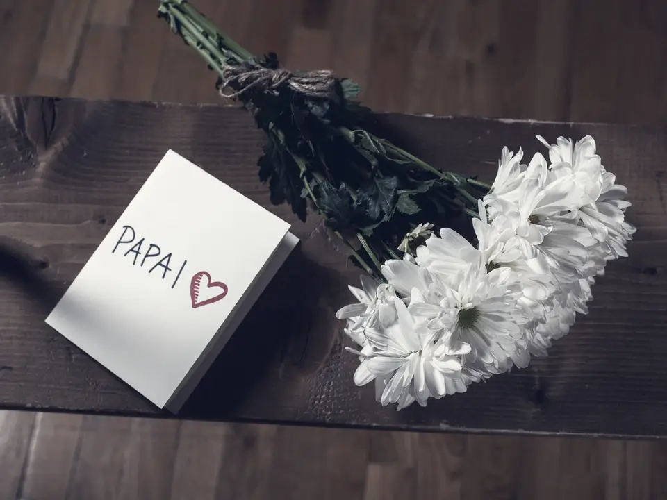 A handwritten greeting card lying next to a bunch of white flowers on a wooden table